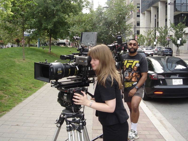 Anna operating a large cinema camera on a city sidewalk