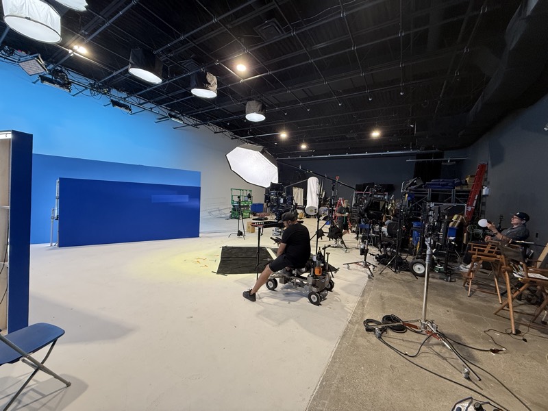 Studio floor with a blue cyclorama, a crew member at the camera cart and lighting stands around them