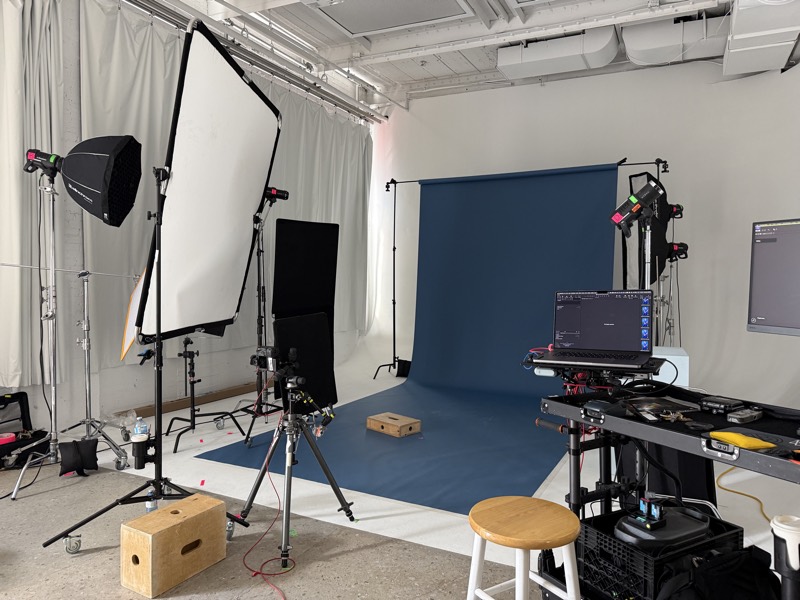 Photo studio set with a blue paper backdrop, two softboxes on stands and a camera on a tripod