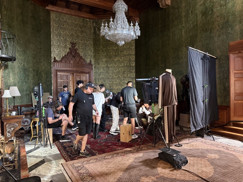 Period interior with green damask walls and a chandelier, crew gathered around the camera