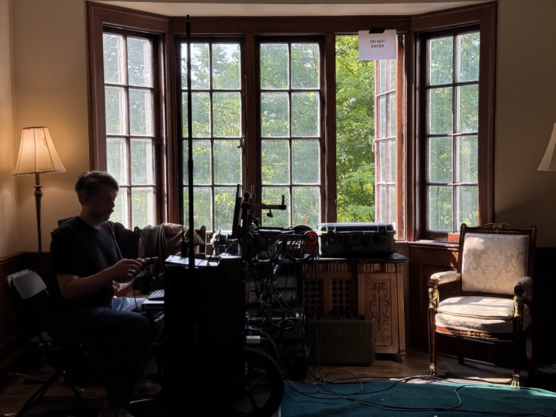 Crew member working beside a bay window, camera gear staged around the room