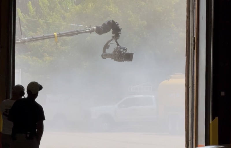 Camera crane arm silhouetted through a doorway in heavy haze