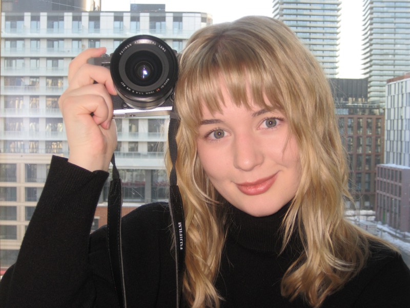 Holding a camera up to frame a shot, the city skyline behind
