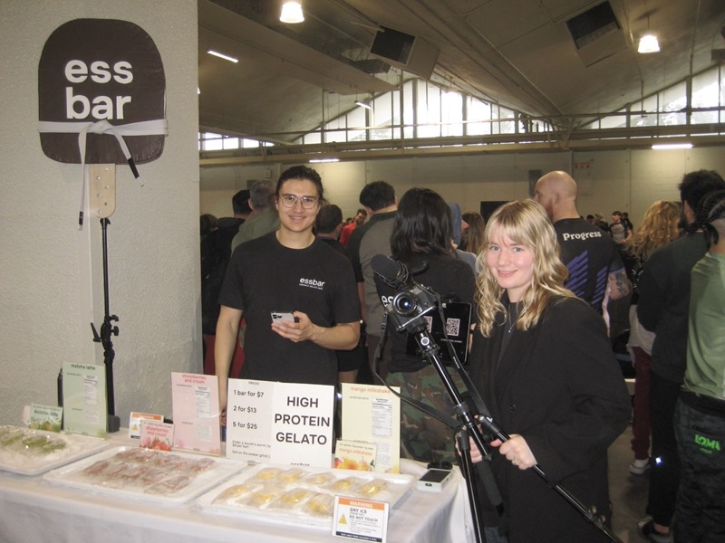 Filming at a trade show stand, the vendor behind the counter mid-conversation