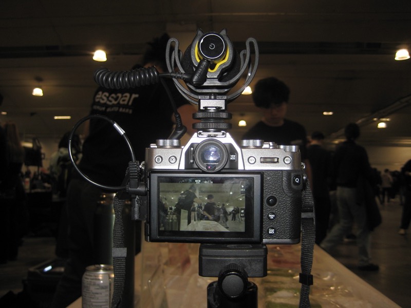 Close-up of a mirrorless camera and shotgun mic on a tripod, the event hall behind